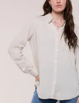 Camisa de lino marca Dash, color beige, con cuello con solapa, escote en V y cierre frontal con botones. Presenta mangas largas regulables con presilla y botón, y un bolsillo aplicado en el pecho.