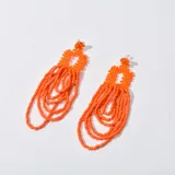Aros colgantes color naranja, con base circular tejida con cuentas y flecos de cuentas colgantes.