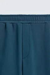 Pantalón jogger de corte relajado y pernera ancha, confeccionado en tejido de algodón con interior perchado. Presenta cintura elástica con cordón interior, bolsillos laterales y un bolsillo trasero de plastrón.