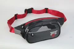 Riñonera con estampado de camuflaje en tonos grises, con logo del equipo de baloncesto Chicago Bulls en el frente. Tiene correa roja ajustable con hebilla de plástico y cierre de cremallera roja.