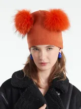 Gorro de lana color naranja con dos pompones grandes de piel sintética en la parte superior.