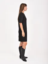 Vestido corto de corte recto y estilo minimalista, confeccionado en tela tipo gamuza negra. Presenta cuello redondo, mangas cortas y dos bolsillos frontales aplicados a la altura de la cadera.