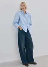 Camisa celeste de algodón y lyocell, con cuello camisero, mangas largas con puños anchos, cierre frontal con botones y sutil bordado floral en el pecho.