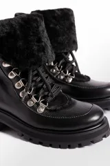 Borcego de cuero vacuno color negro, con interior forrado en corderito sintético. Presenta cordones negros, ganchos metálicos plateados y suela de goma tipo track con plataforma.