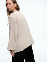 Sweater de punto color gris, con cuello redondo, mangas largas acampanadas y diseño holgado con costuras visibles.