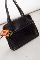 Cartera de hombro tipo portafolio confeccionada en cuero vacuno, con diseño estructurado que combina marrón liso y un panel frontal en cuero texturizado color mostaza. Posee doble asa larga y cierre superior.