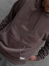 Canguro con capucha y cordones ajustables, color marrón con efecto lavado. Presenta un bolsillo frontal tipo canguro y el logo de la marca Osten estampado en el centro del pecho.