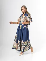 Conjunto de dos piezas confeccionado en viscosa con estampado floral en tonos marrones y verdes sobre base blanca. Incluye una blusa tipo camisa corta con cuello solapa, cierre frontal de botones y mangas abullonadas con diseño globo, y un pantalón tipo culotte de tiro alto, amplio y fluido con pinzas en la cintura.