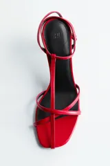Sandalias rojas de taco fino y alto, con diseño de tiras finas en el empeine, tira en T y pulsera ajustable con hebilla en el tobillo.