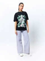 Remera negra de manga corta, corte oversize, con estampado frontal de una figura femenina de estilo asiático rodeada de flores blancas y verdes.