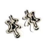 Par de aros colgantes con forma abstracta irregular, hechos de acrílico blanco con diseño interior de manchas negras y plateadas con glitter.