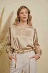 Blusa de satén color champagne con cuello a la base, mangas anchas y puños elásticos con detalle bordado.