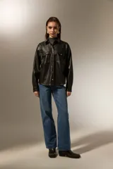 Sobrecamisa de cuero sintético en color negro, con cuello clásico, cierre frontal mediante botones metálicos y dos bolsillos frontales con solapa. Presenta costuras a la vista y mangas largas con puños abotonados.