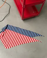 Pañuelo triangular tejido con diseño de rayas. Una sección presenta rayas horizontales en tonos azul y marrón, mientras que la otra sección presenta rayas horizontales en tonos rojo y beige.