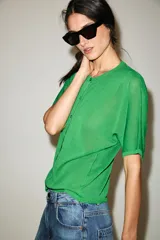 Chaqueta de punto de manga corta y cuello redondo en color verde, con cierre frontal de botones.