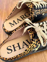 Sueco tipo zapatilla con diseño destalonado, confeccionado en cuero con estampado animal print de leopardo. Presenta cordones en tono beige y suela plana negra.