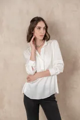 Blusa blanca de manga larga con cuello camisero y cierre frontal parcial con botones.