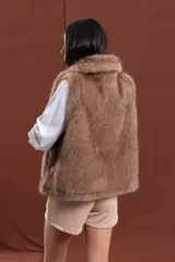 Chaleco de piel sintética en color marrón, con diseño de corte recto y largo a la cadera. Presenta un cuello amplio con caída envolvente y cierre frontal oculto, con interior forrado.