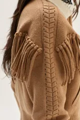 Bomber de tejido de punto color camel, con cuello de lana merino, cierre frontal, flecos decorativos en el frente y la espalda, y detalle de trenzas en las mangas.