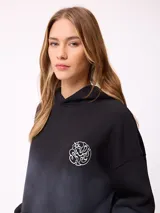 Canguro oversize color negro con efecto degradado, capucha, bolsillo frontal tipo canguro y puños elásticos. Presenta un parche con logo en la manga.