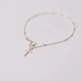 Pulsera tipo denario confeccionada en plata 925, compuesta por una cadena fina con pequeñas esferas intercaladas y un dije colgante en forma de cruz.