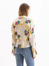 Camisa de seda color beige con estampado colorido de frutas, cuello camisero, mangas largas y ajuste elástico en la cintura.