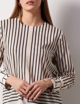 Blusa de gasa estampada con líneas verticales negras sobre fondo beige, de manga larga con puño abotonado. Espalda con abertura y botón.
