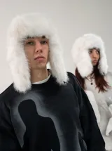 Gorro tipo ushanka de peluche blanco, con orejeras largas y forro interior. Cuenta con un sistema de cierre mediante clip.