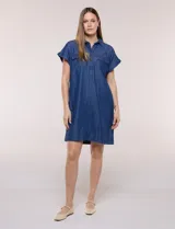 Vestido camisero corto de jean color azul, con cuello camisero, escote en V y botones frontales parciales. Tiene mangas cortas con dobladillo y bolsillos con solapa en el pecho.