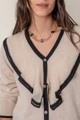 Cárdigan negro de punto fino con hilos de lurex, cuello en V calado con volados color crema, cierre frontal con botones con strass y puños anchos con ribete color crema.