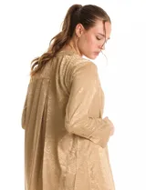 Túnica satinada color dorado con estampado animal print, de silueta oversize y fluida, largo maxi. Cuello a la base con abertura central y botones a tono. Manga larga de corte recto con puños amplios y cierre de botones. Espalda con canesú horizontal recto del cual nace un tablón central profundo. Bajo asimétrico redondeado con tajos laterales profundos, el largo de espalda mayor al largo delantero.