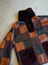 Buzo de cuero genuino con diseño de patchwork en cuadros de colores negro, marrón y bordó. Presenta cuello alto y bolsillos frontales con detalle de piel sintética en color bordó.