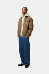 Campera Carhartt WIP modelo Detroit Jacket, de color marrón con cuello corduroy negro y cierre frontal de cremallera. Presenta un bolsillo con cierre en el pecho con el parche del logo de la marca.