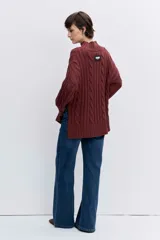 Sweater de punto con diseño de trenzas, cuello alto y mangas largas con puños acampanados. Presenta un corte holgado con terminación asimétrica en el ruedo.