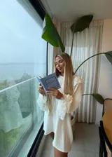 Vestido corto color crudo con diseño holgado, cuello redondo y mangas largas con puños acampanados. Presenta detalles de encaje floral en el cuello y en los puños de las mangas.