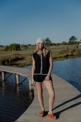 Conjunto de dos piezas tejido en algodón, compuesto por un chaleco sin mangas con cierre frontal de botones y un short de tiro medio. Ambas prendas presentan un diseño en color blanco con detalles de terminaciones en color beige.