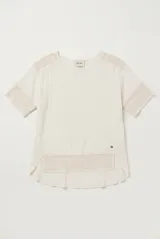 Blusa color blanco, de corte holgado y mangas tres cuartos, con detalles de encaje y bordados en las mangas y en el ruedo.