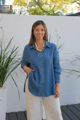 Camisa de jean de corte oversize, con cuello clásico, cierre frontal de botones y mangas largas. Presenta un diseño con bolsillos laterales integrados y ruedo redondeado.