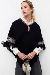 Poncho artesanal de lana en color negro, con diseño de guardas geométricas en tonos beige y blanco en los bordes y flecos decorativos en todo el contorno.