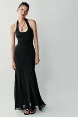 Vestido largo negro de cuello halter, espalda descubierta y escote redondo. Presenta un diseño de punto combinado en la parte superior y una falda larga de tejido fluido.
