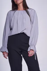 Blusa de manga larga color rosado, con cuello redondo y puños elásticos con volados y lazos decorativos. Presenta un diseño holgado con frunces en el escote.