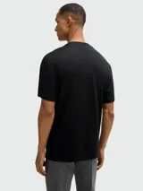 Remera de algodón negra con cuello redondo y manga corta. Presenta un estampado frontal con el logo de la marca en color verde sobre un diseño de franjas verticales con efecto de nubes.