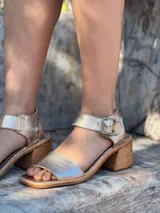 Sandalias de cuero color dorado con pulsera al tobillo y hebilla metálica. Taco bajo de madera.