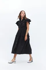 Vestido midi de lino blanco con diseño de broderie, cuello alto, cierre frontal con botones y volados decorativos en los hombros y el cuerpo.