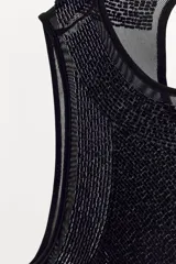 Top negro sin mangas, con cuello redondo y abertura con botón en la espalda. Presenta un detalle de abalorios a tono en el borde del cuello y sisas.