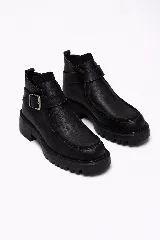 Bota corta tipo borcego de cuero negro con textura granulada, suela track dentada y tira decorativa con hebilla metálica en el tobillo.