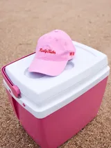 Gorra de lona color crema con visera celeste. Presenta bordado frontal en hilo azul claro con el texto "Rusty Tribe" y un pequeño diseño de flores.