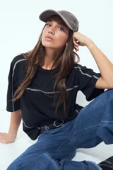 Remera de manga corta con silueta relajada y costuras a la vista en color blanco que contrastan sobre el tejido negro. Presenta un diseño moderno con terminaciones destacadas.