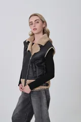 Chaleco sin mangas de cuero sintético negro con interior y detalles de piel sintética en color beige. Presenta cierre frontal asimétrico, cuello solapa y correas ajustables en la cintura.