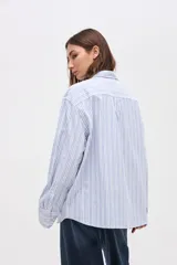 Camisa de corte oversize con diseño de rayas verticales finas en tonos claros. Presenta cuello clásico, cierre frontal con botones y mangas largas con puños abotonados.